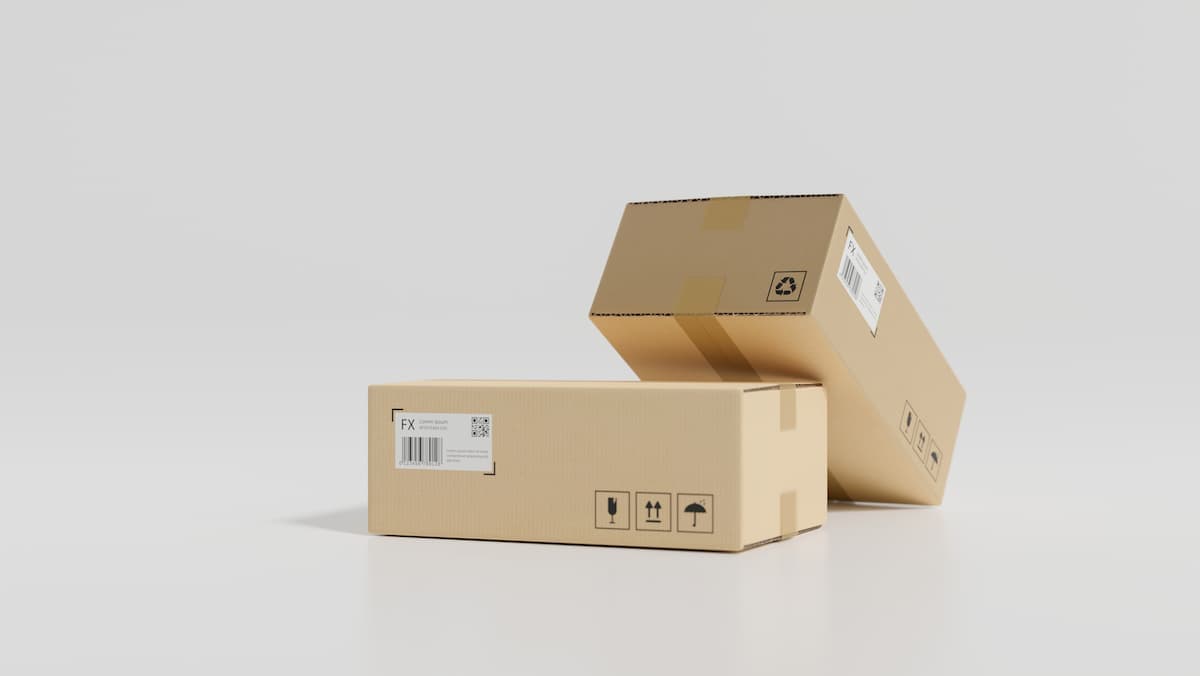 Pressure-sensitive adhesive how to choose: two cardboard shipping boxes with barcode labels and handling symbols on a clean studio background.