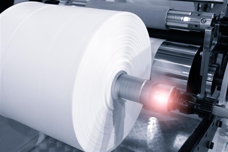 Large industrial roll of white paper or film material on a production machine in a manufacturing facility.