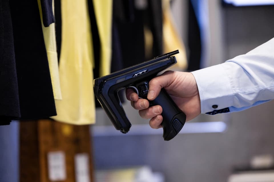 Passaporte digital de produto (DPP) sendo verificado com leitor portátil em itens de vestuário no ponto de venda, garantindo rastreabilidade e informações do produto.