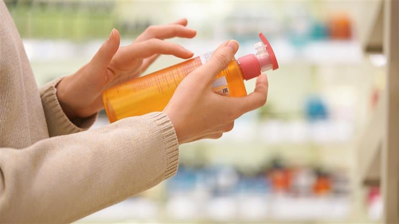 Hands holding an orange pump-top cosmetic bottle, examining the label in a store aisle.