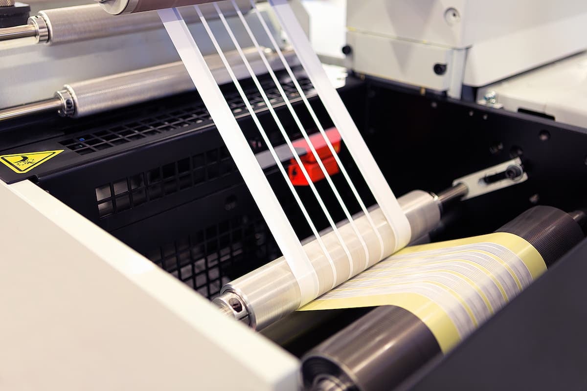 Pressure-sensitive label web being slit into narrow strips on an industrial converting press.