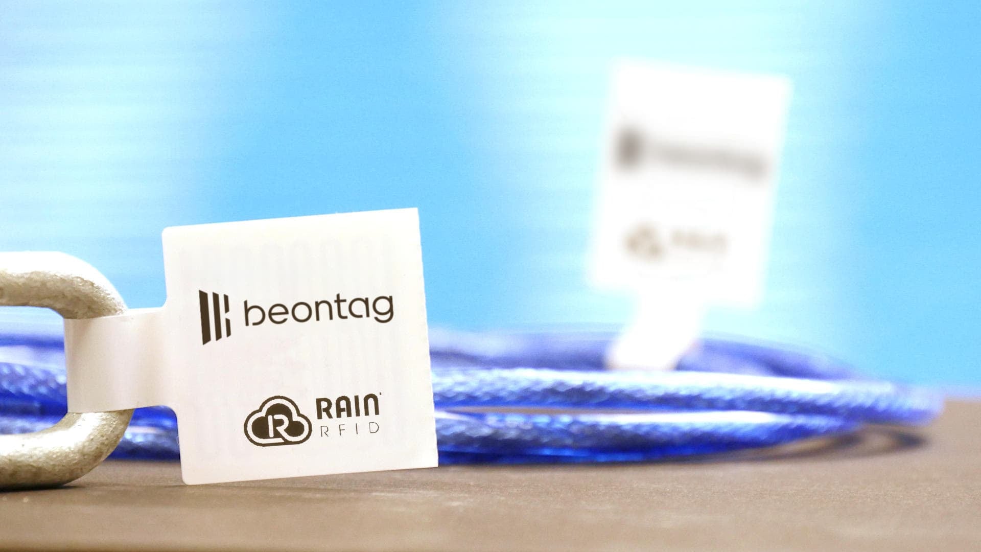 Close-up of a Beontag RAIN RFID loop tag attached to a metal link, with a blue cable in the background.