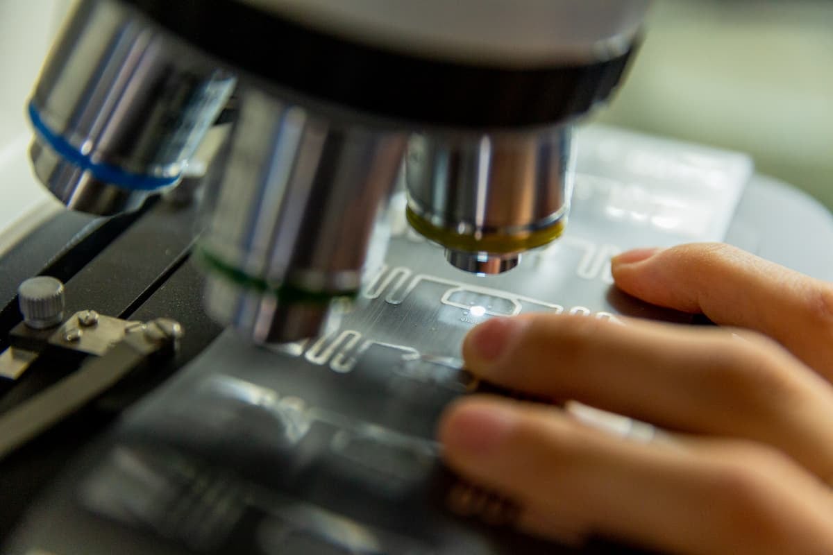 Microscope inspecting an RFID tag antenna on a transparent substrate, technician holding the sample.