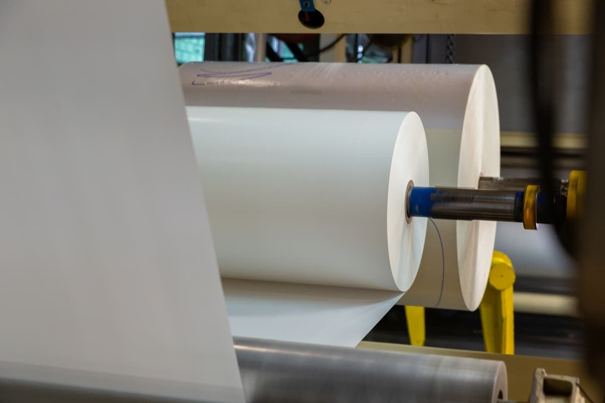 How to choose pressure-sensitive adhesive: large rolls of release liner material running through converting equipment in a production line.